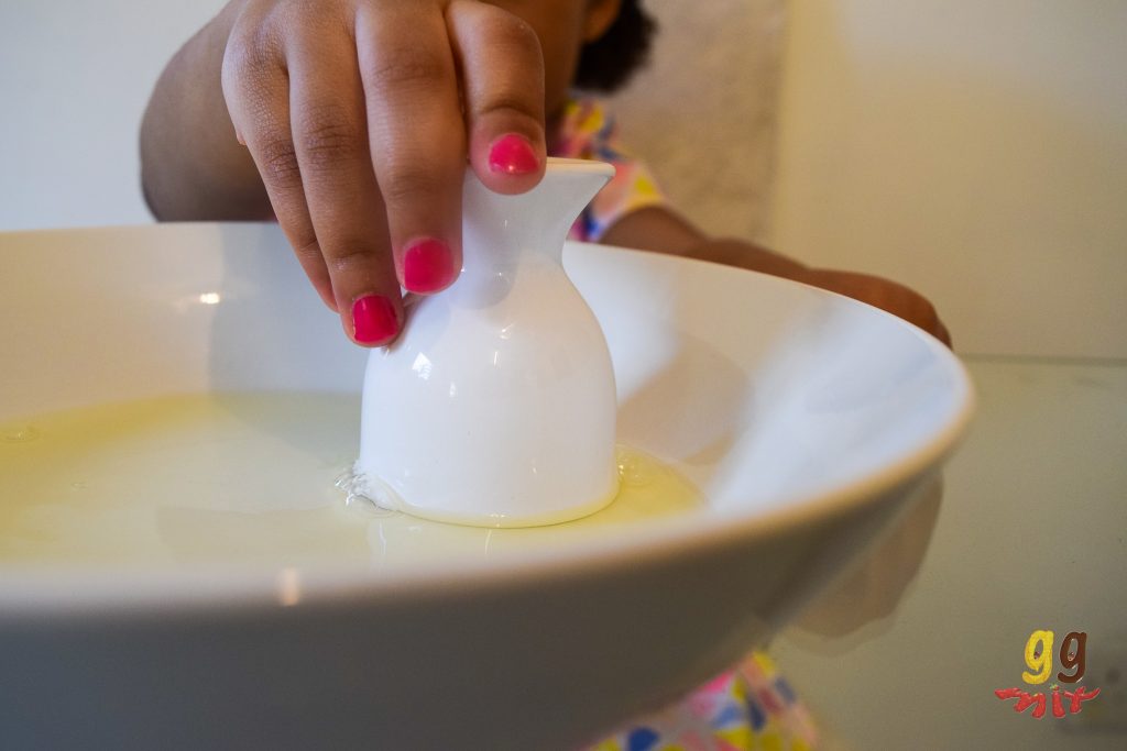 a hand holds a white egg cup upside down in a white bowl fillef with egg whites