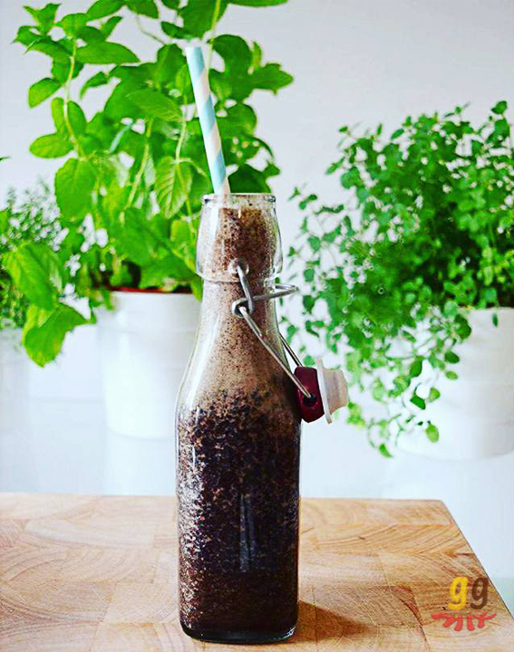 Healthy blueberry, banana, spinach and cinnamon green smoothie drink in a glass bottle with a striped blue and white straw and herbs in the background ggmix