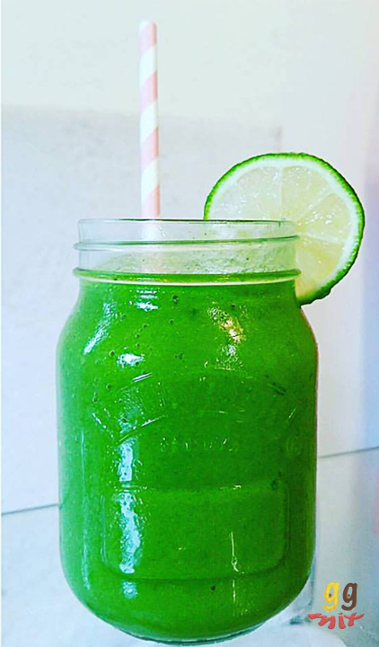 Healthy mango, pineapple, banana, spinach and mint green smoothie drink in a jar with a lime slice on the top and a pink and white straw ggmix