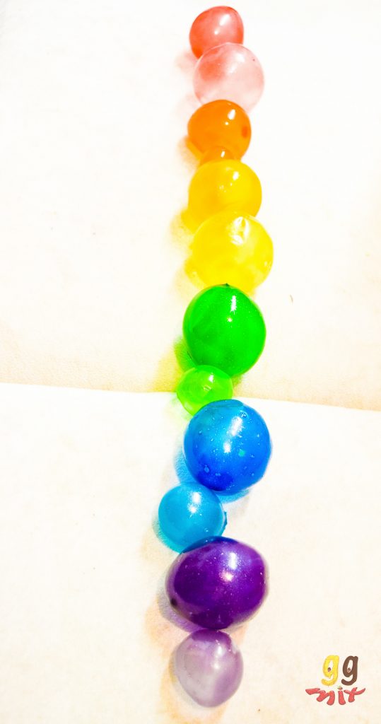 a row of rainbow gelatin bubbles coloured red, orange, yellow, green, blue and purple on a white background