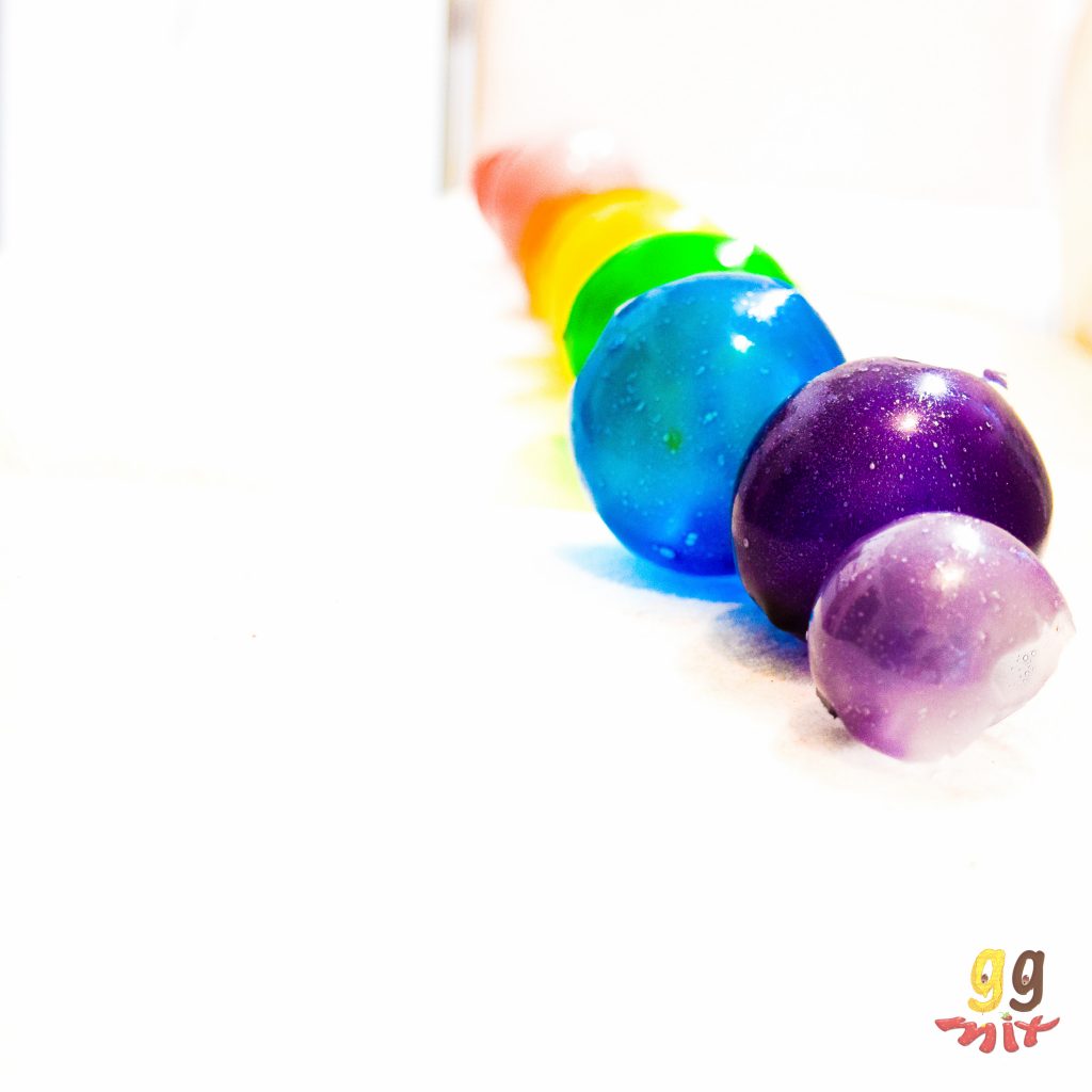 a row of rainbow gelatin bubbles coloured red, orange, yellow, green, blue and purple on a white background