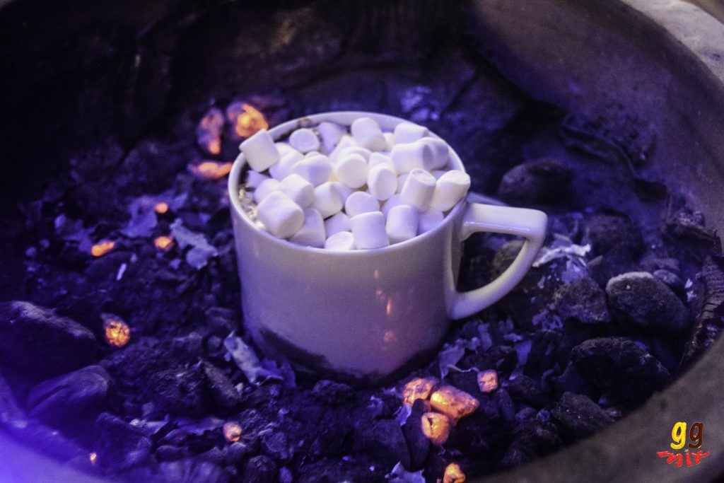 a cup of hot chocolate topped with marsmallows sitting on a charcoal bbq