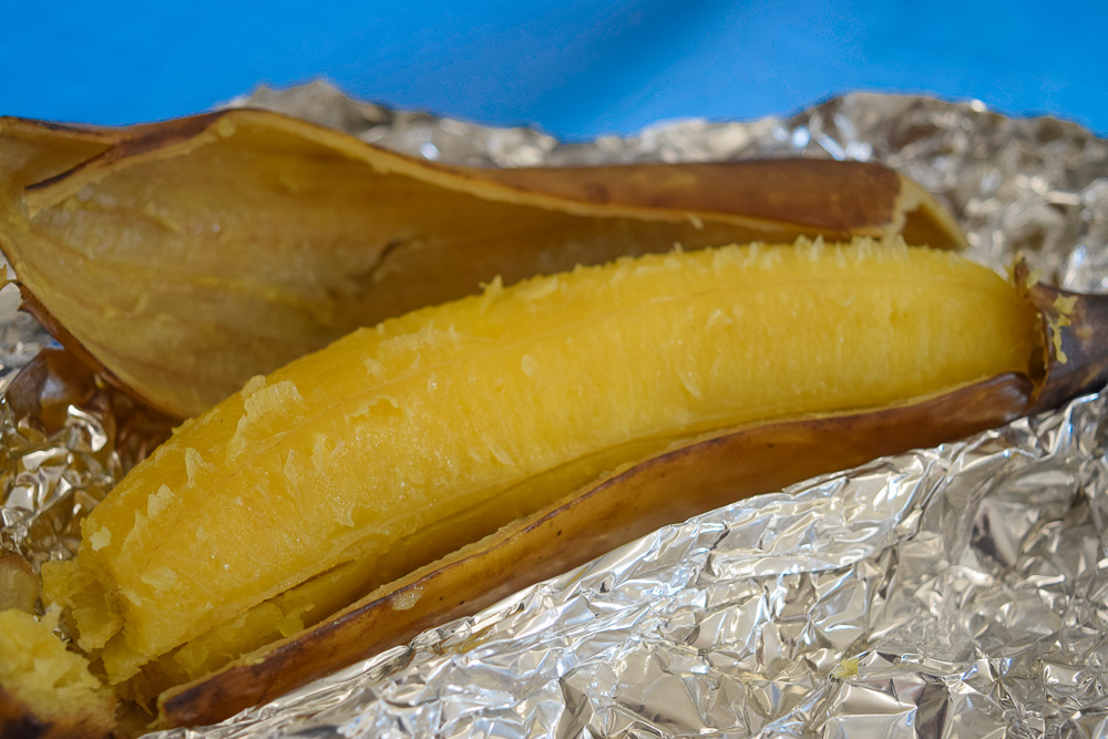 baked plantain still in its skin but half peeled sitting on foil