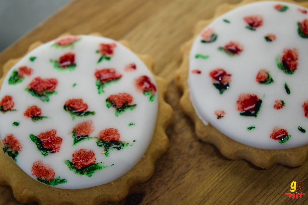 cookies covered with white fondant that has red roses with green leaves painted on it